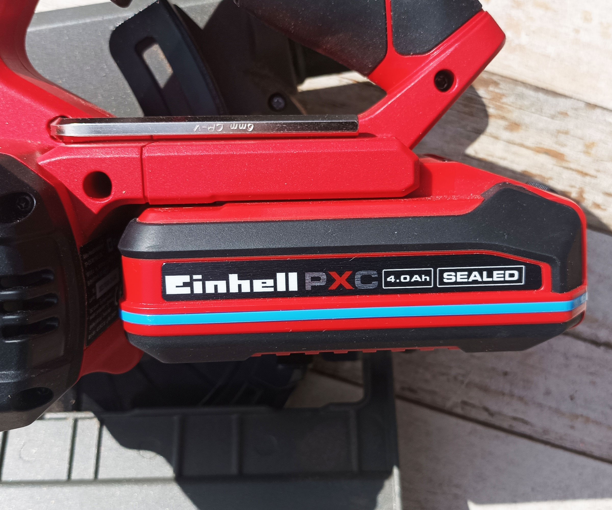 Red and black Einhell PXC battery attached to Einhell circular saw on whitewashed wood