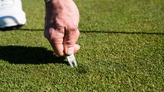 A golfer repairing a pitch mark