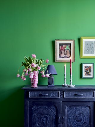 Bright green wall with navy painted set of drawers with pink flowers and photo frames