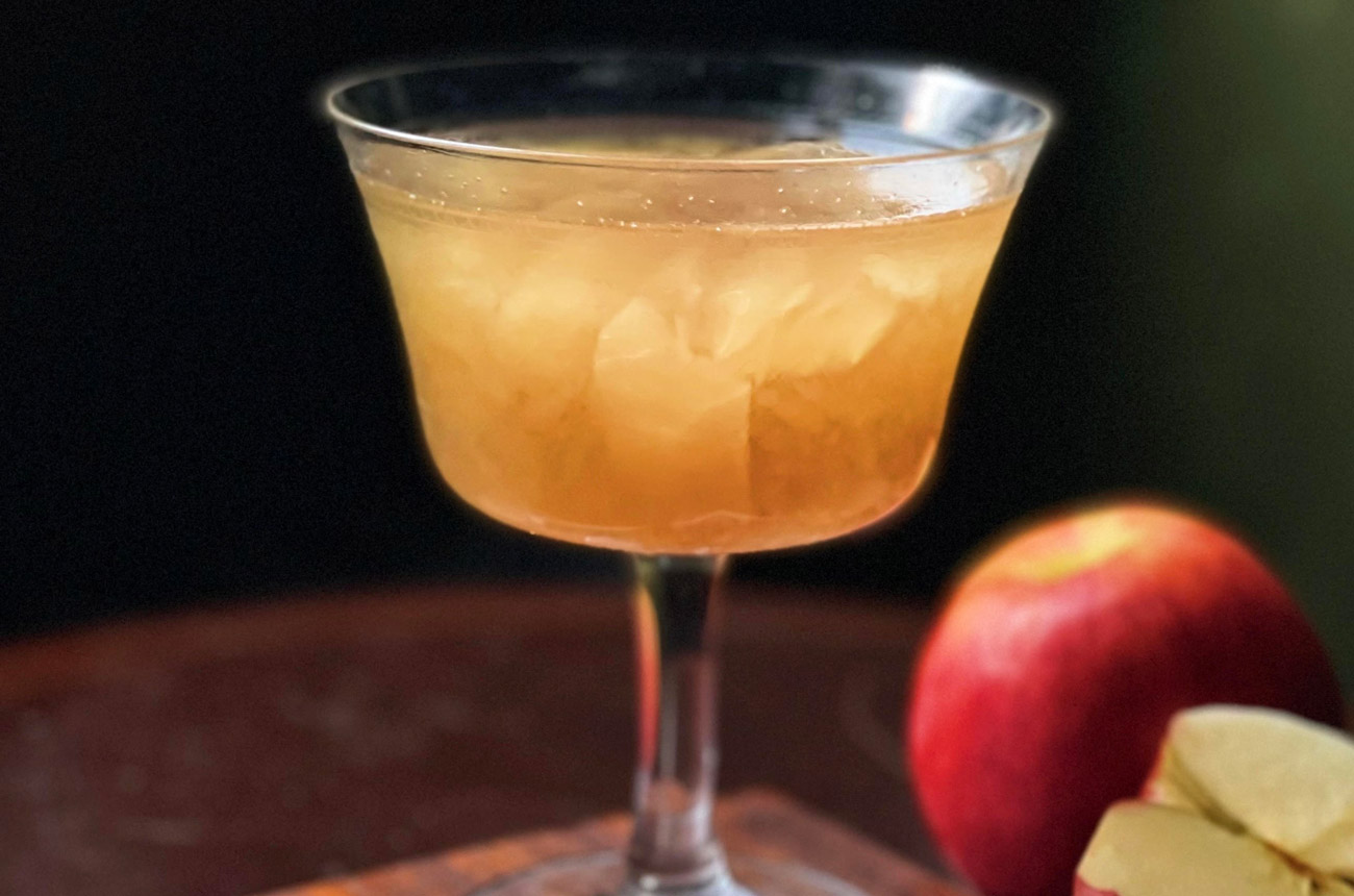 A cocktail in a coupe glass next to apples