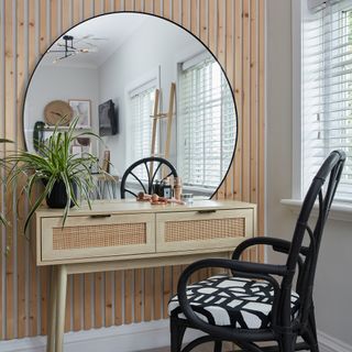 Rattan dressing table with round mirror in front of panelled wall