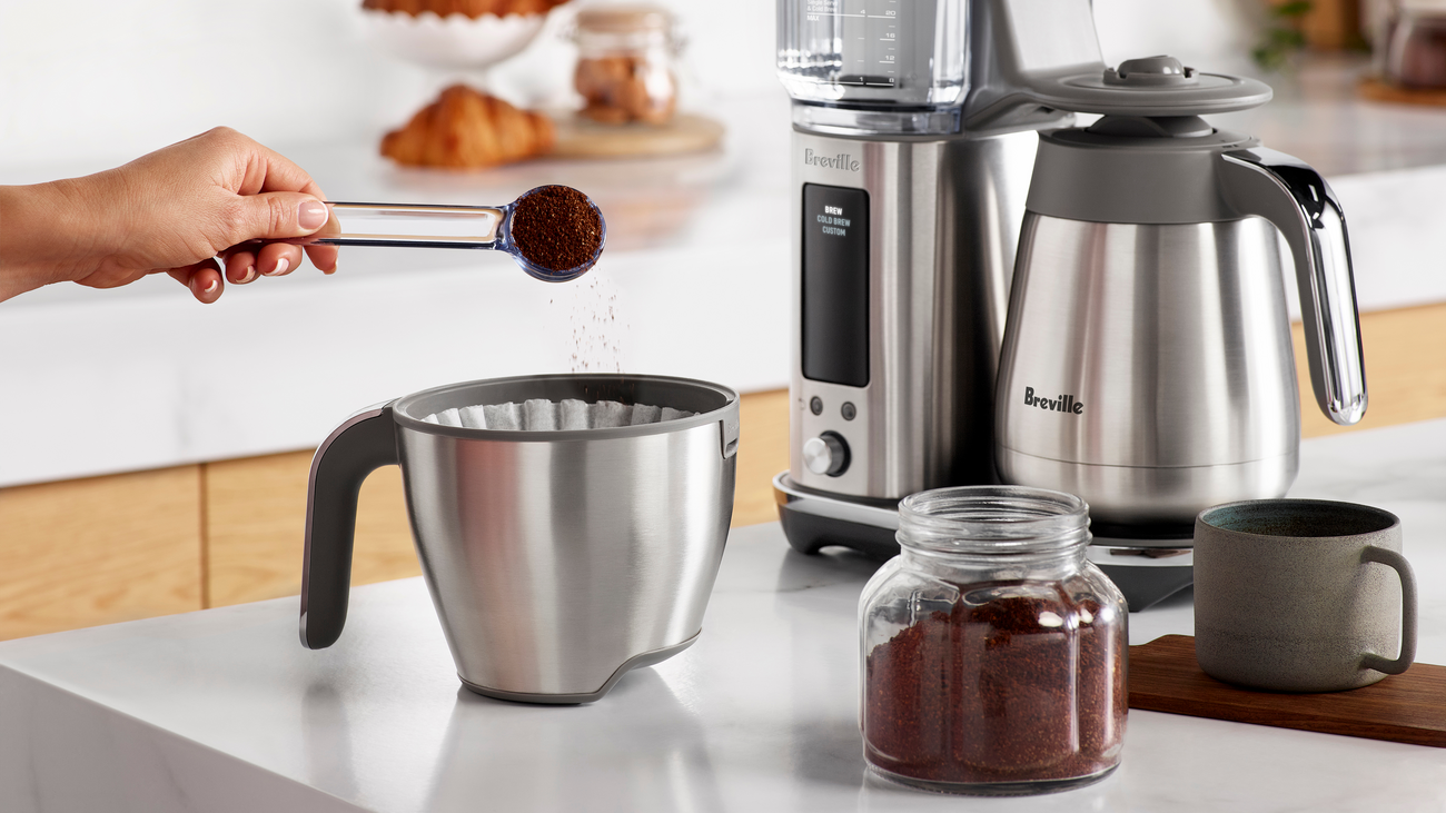 Person adding ground coffee to Breville Luxe Brewer coffee maker
