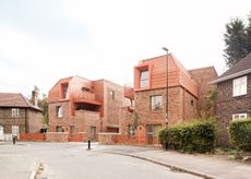 view of Farmstead Road, a brick community housing residential complex in south london by metropolitan workshop. it features green gardens and orange metal details such as window frames and balconies