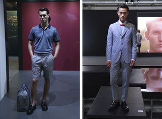 Two side-by-side photos of male models wearing looks from Brioni's collection. In the first photo the model is wearing a blue patterned top, light coloured shorts, black shoes and has a bag on the floor next to him. In the second photo the model is wearing a white shirt, a grey top with dark red along the neckline, a grey suit and black shoes. In the background there is a person facing the opposite direction and an image of a man's face showing on a large screen