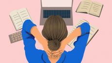 High angle view of a female office worker with hands around back of neck with laptop and books scattered around a desk.