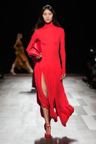 Ferragamo model wearing a red turtleneck drop-waist dress and carrying a red bag at the F/W 24 show.