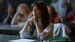 A press photo of Jenna Ortega sitting at a desk leaning her chin against her hands in Miller's Girl.