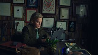 Ronan Farrow types on a computer in front of a wall of framed certificates, in 'Surveilled.'