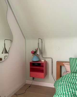 A green bed next to a pink nightstand and blob mirror