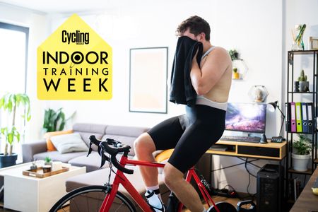 A cyclist on a turbo trainer with a towel over his face