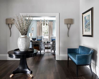hallway paint ideas, grey painted hallway with table and blue sofa, open plan layout with blue painted living room in the background
