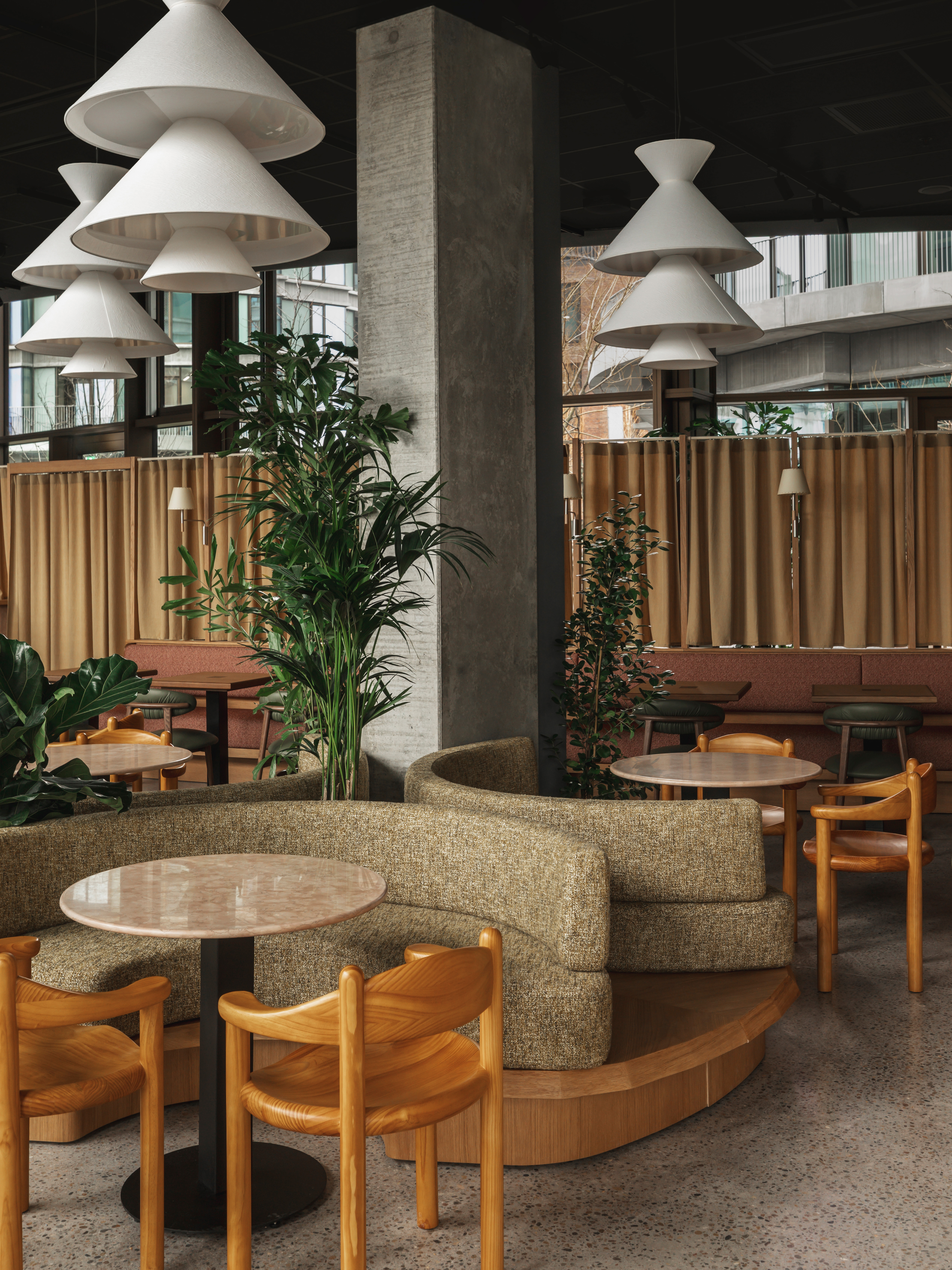 A brutalist shell of a hotel where cement walls and tall ceilings are softened by warm woods, textural fabrics, soft forms, and pendant lighting in earthy tones.