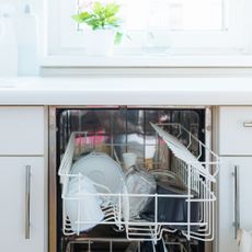 Integrated dishwasher with open door and neatly stacked crockery in white kitchen
