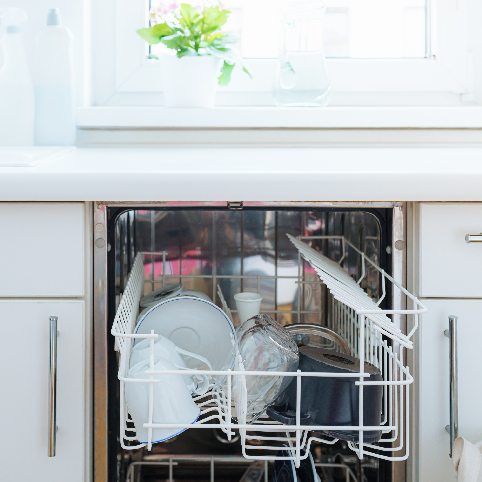 Integrated dishwasher with open door and neatly stacked crockery in white kitchen