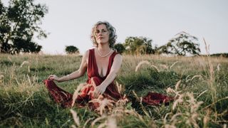 A photo of Mangala Holland, sexual empowerment coach, wearing a red dress and sitting in a field