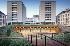 The campus featuring an outdoor stair case that leads down to a lower level with glass windows and doors. Behind that at street level are two nine-floor buildings parallel to one another. 