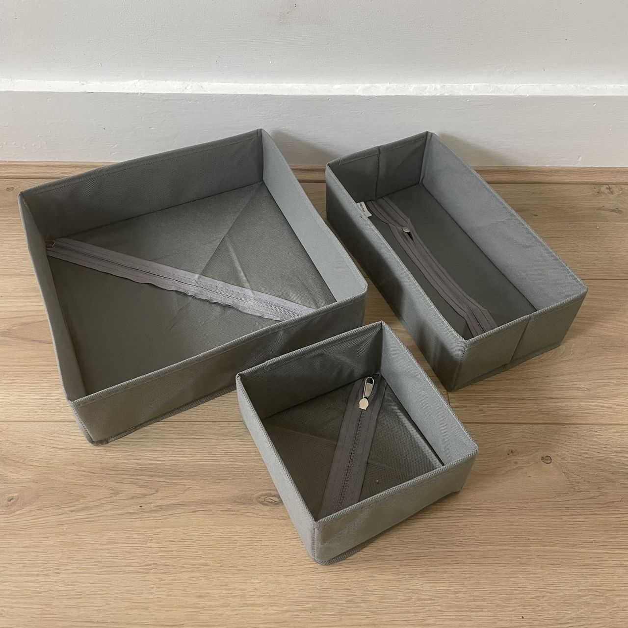Three grey clothes organisers sitting on wood-effect flooring in front of a white wall