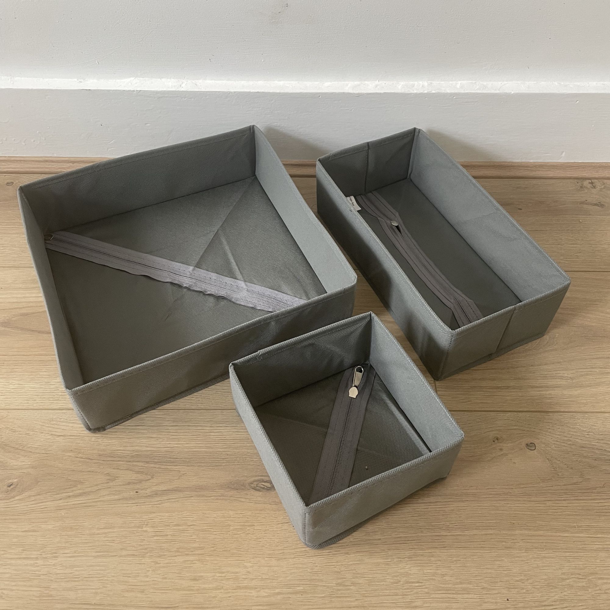 Three grey clothes organisers sitting on wood-effect flooring in front of a white wall