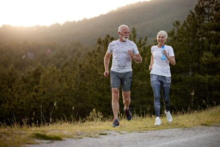 Happy mature couple running during sports training in nature.