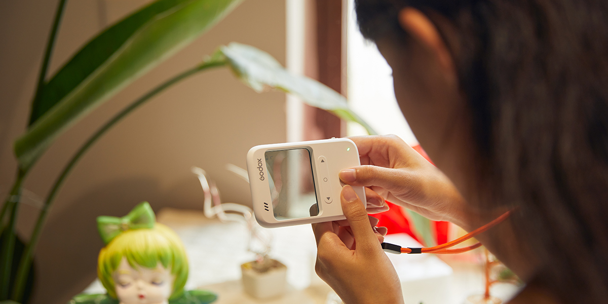 Woman holding Godox C100 transparent window camera and using it to take a photograph of a plastic doll