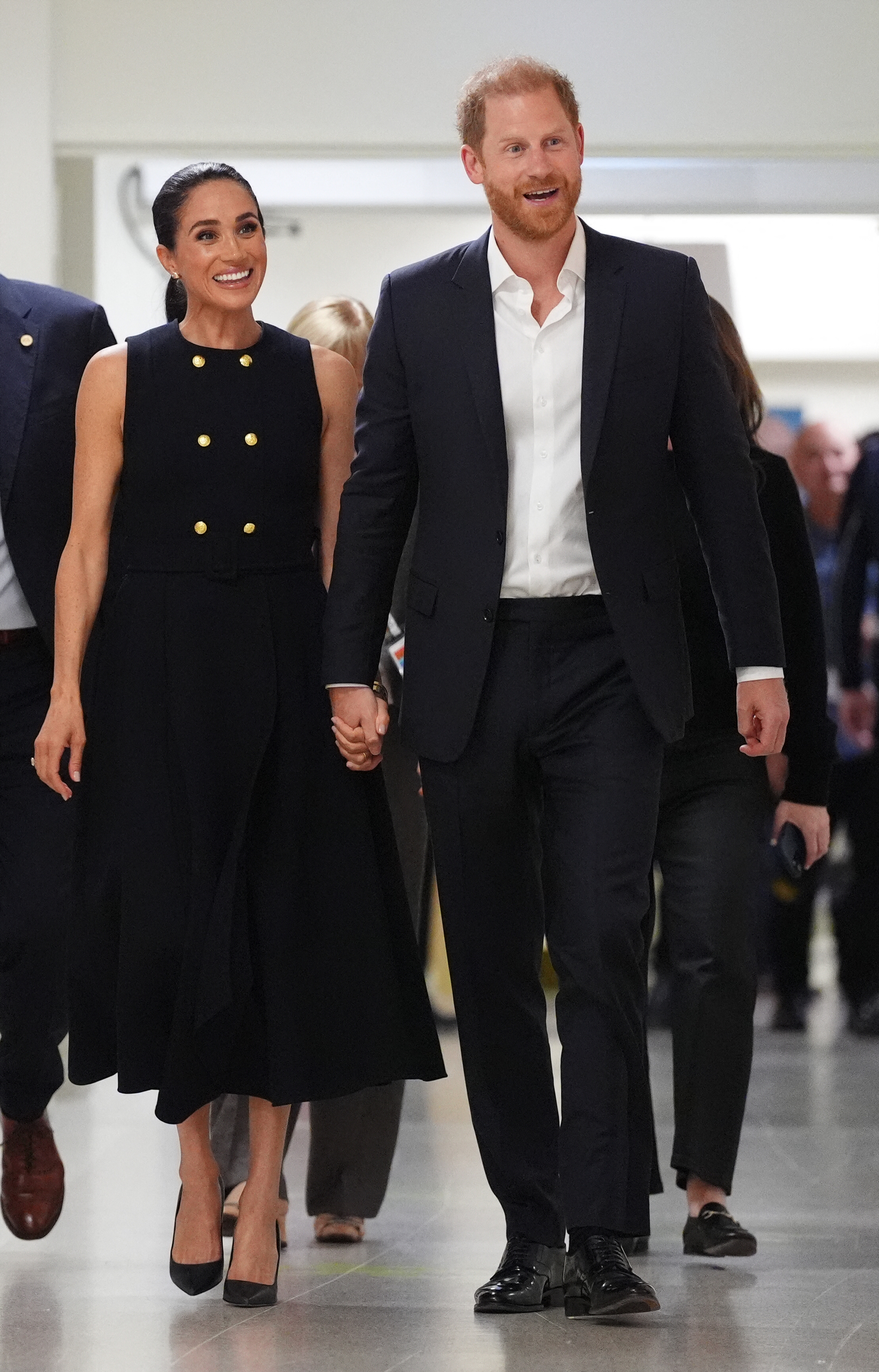Meghan Markle in a black dress holding hands with Prince Harry