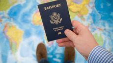 picture of a man holding a U.S. passport while standing on a map of the world