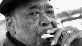 A monochrome close-up of James Cotton playing the harmonica