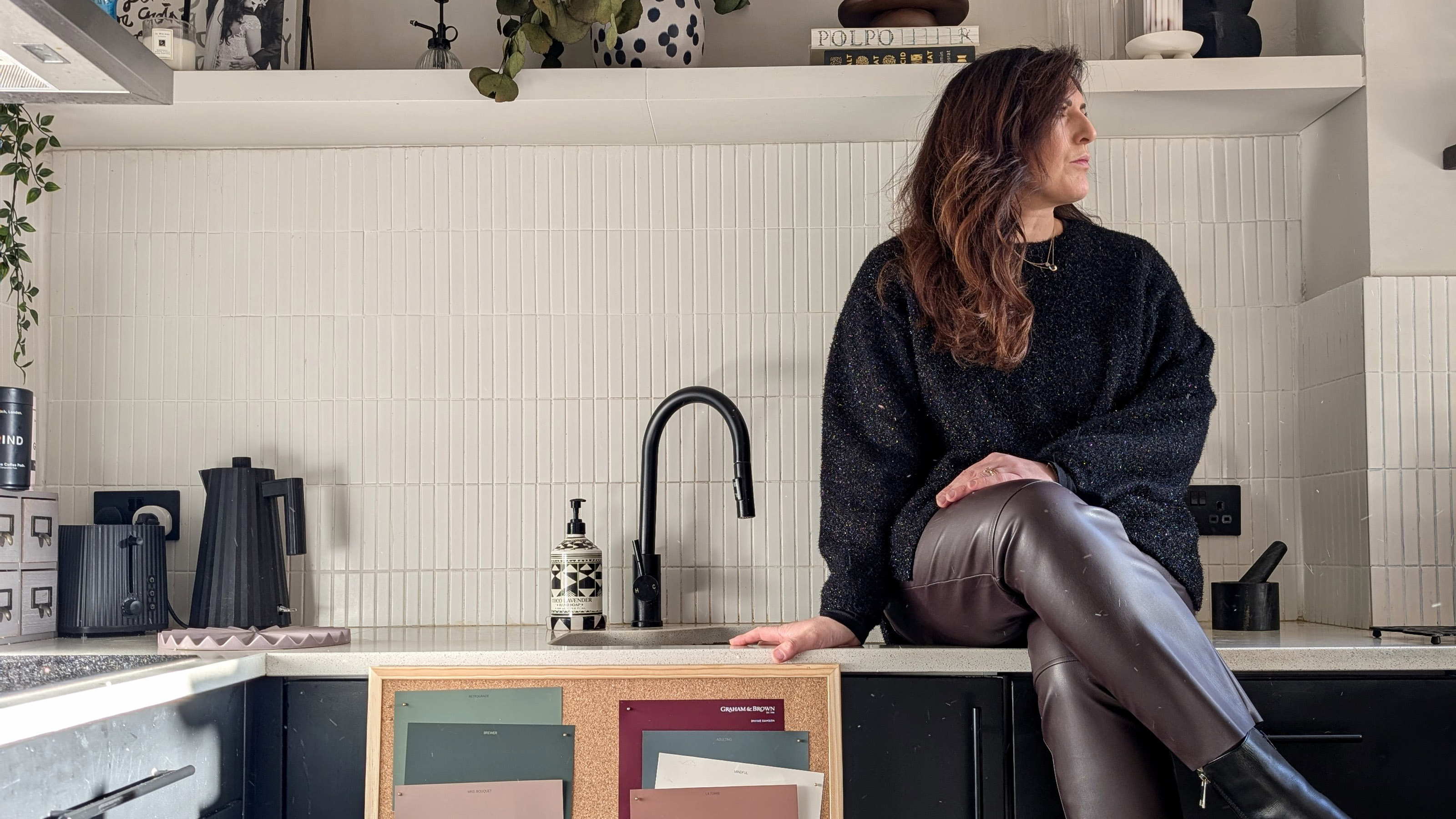 Natalie Jahangiry sat on her kitchen work tops with a board of colour swatches to consider