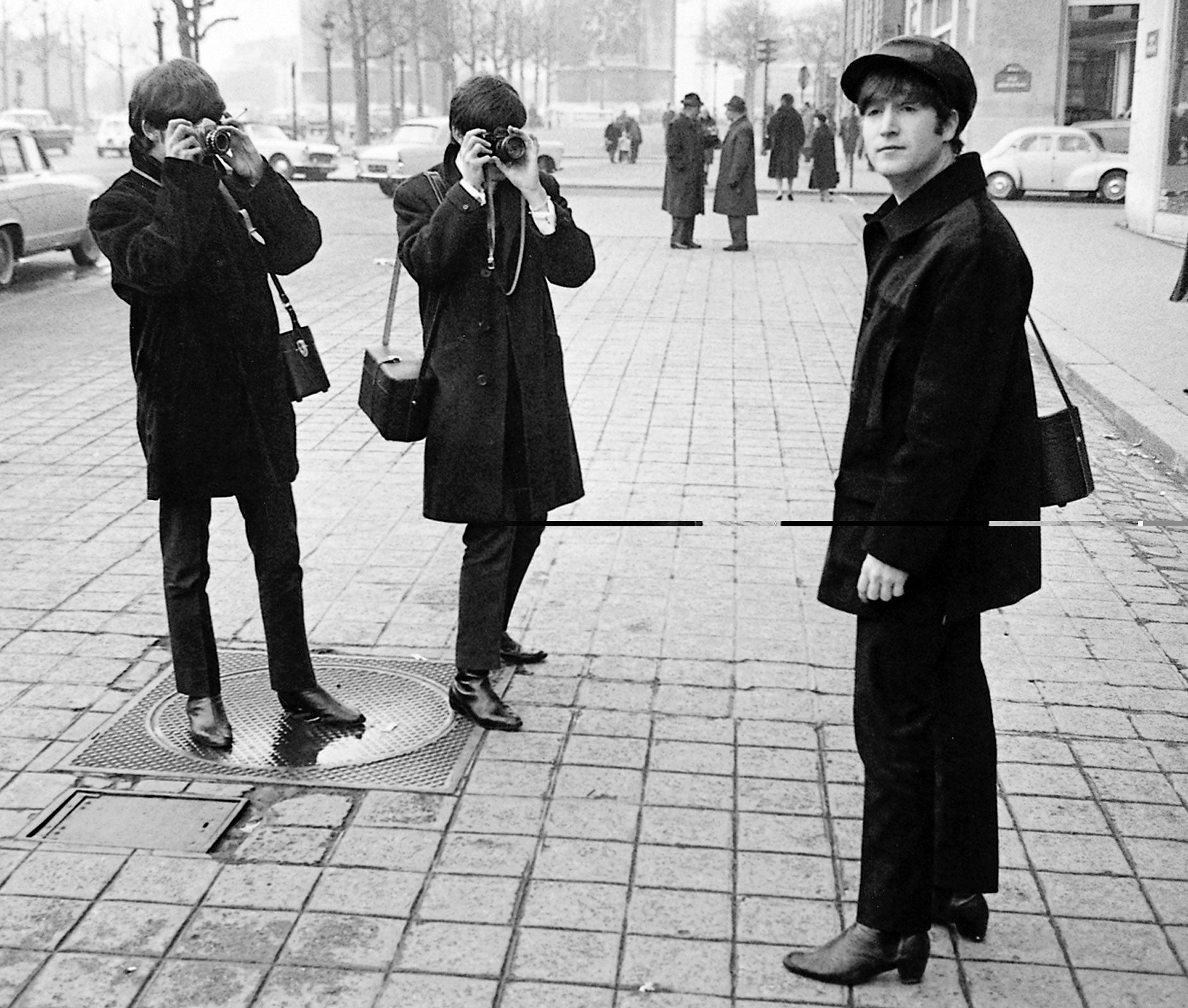 The Beatles on the Champs Elysees before Ringo arrived in Paris later in the day, Wednesday 15th January 1964. George Harrison (left) and Paul McCartney taking pictures as John Lennon looks on. 15th January 1964. (Photo by Alisdair Macdonald/Daily Mirror/Mirrorpix via Getty Images)
