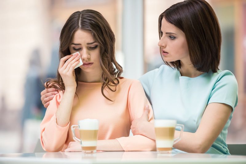 Two women sit together, one consoling the other.