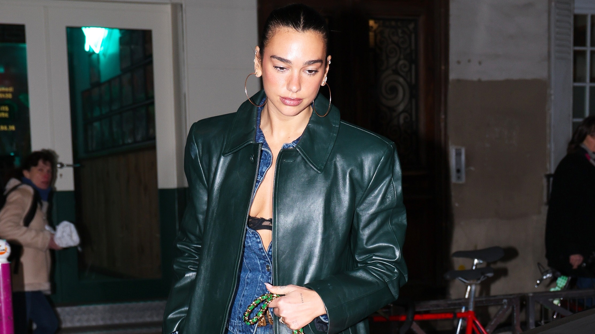 Dua Lipa wearing a long green leather coat, denim jumpsuit, kelly green Chanel 25 bag, and furry brown boots