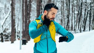 Man checking sports watch while running in snow