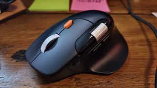 A ProtoArc EM25 ergonomic wireless mouse on a wooden desk, in front of some brightly-coloured post-it notes