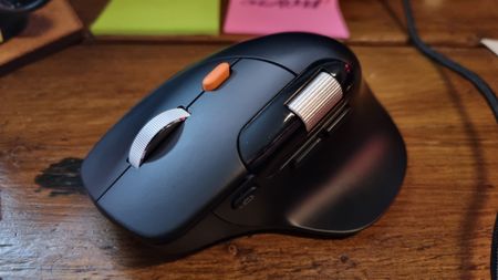 A ProtoArc EM25 ergonomic wireless mouse on a wooden desk, in front of some brightly-coloured post-it notes