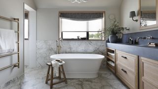 bathroom with marble tiles, wooden cabinets, black countertop, freestanding white bath