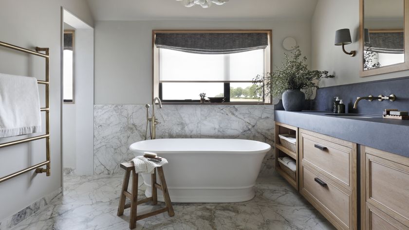 bathroom with marble tiles, wooden cabinets, black countertop, freestanding white bath