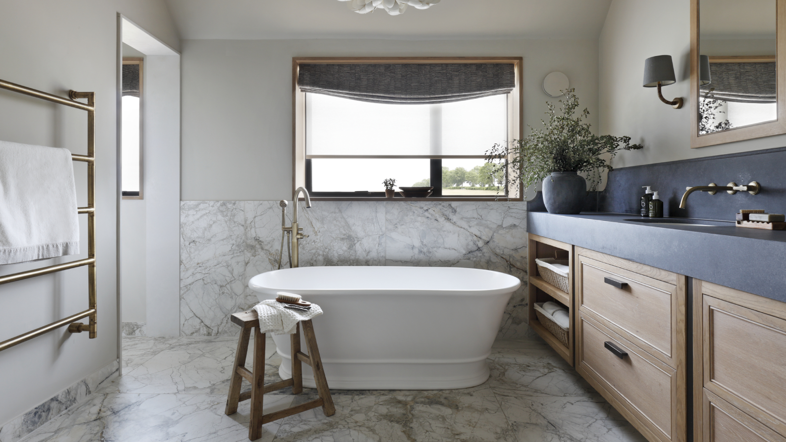 bathroom with marble tiles, wooden cabinets, black countertop, freestanding white bath