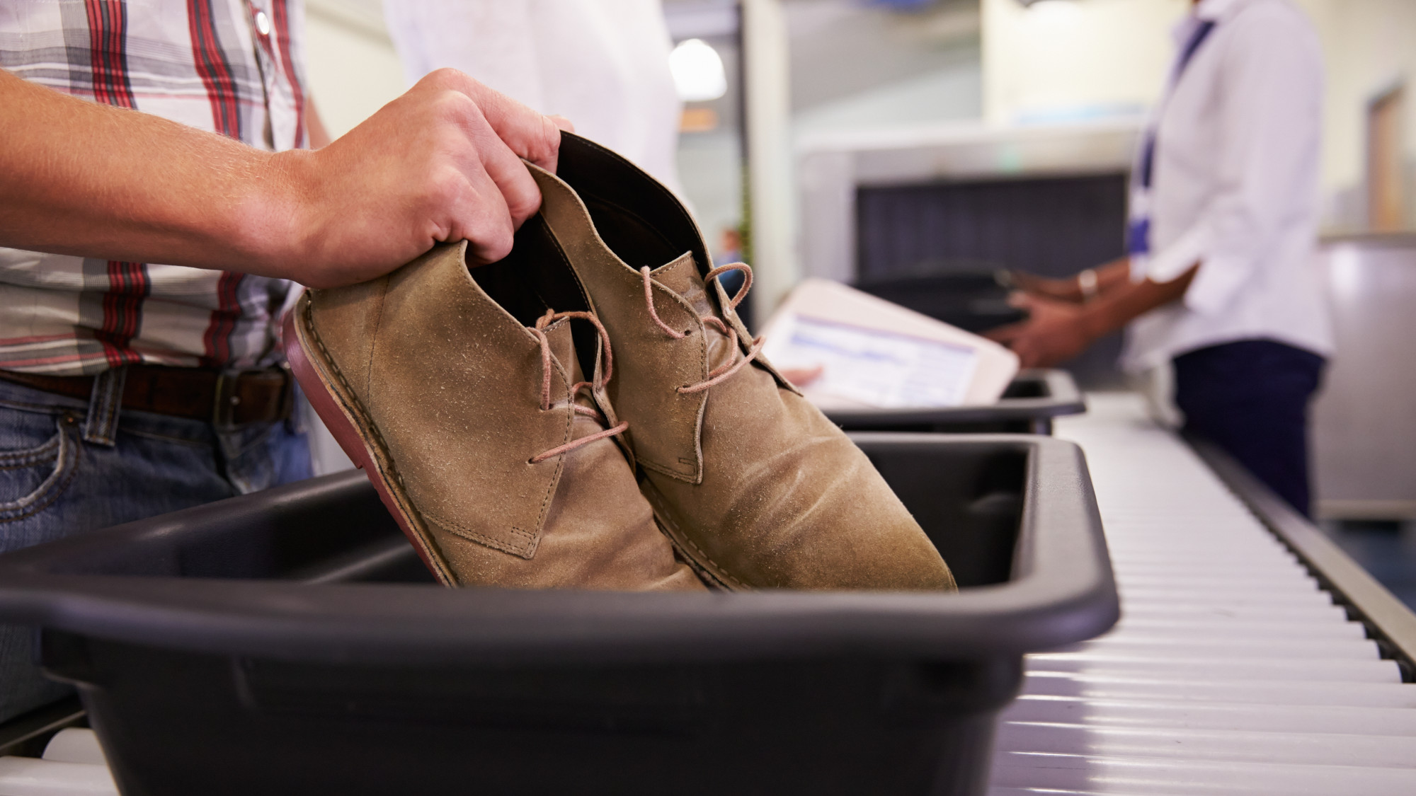 A man putting shoes into a tray at the airport