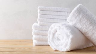 Four white towels stacked and rolled on a wooden surface