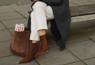 Anouk wears white jeans, a gray long coat, brown suede kitten heels, and a brown suede bag.