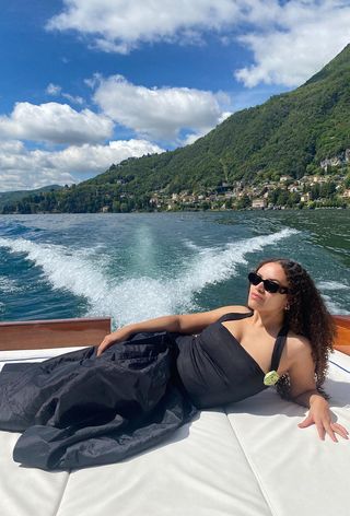 a photo showing what to wear on a boat with a woman wearing black sunglasses, silver hoops, a black halter top, and a black a-line full skirt