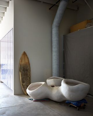 Gregory's Christiansen surfboard leans on a studio wall behind his Triclops pendant light