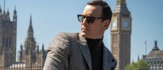 Michael Fassbender leans in front of the London skyline while wearing sunglasses and a suit in Black Bag.