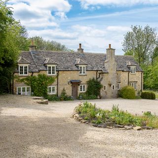 stone wall house with brown roof white windows and plants in yard