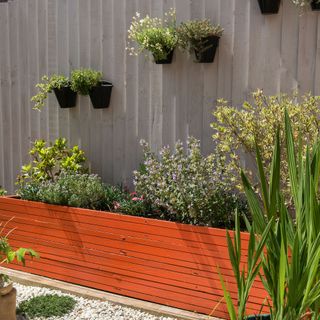 Rust coloured raised planter with wall hung plant pots