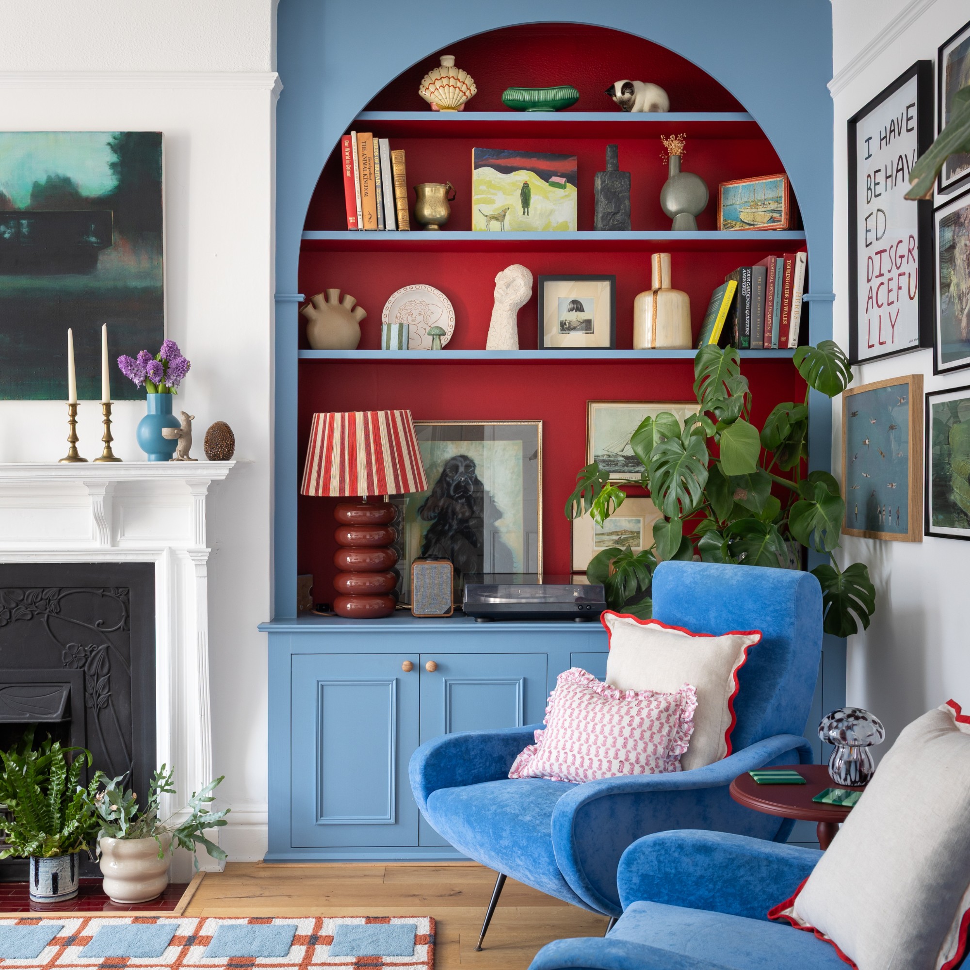 A living room painted in white with an arched alcove bookcase painted in a sky blue with a warm red interior