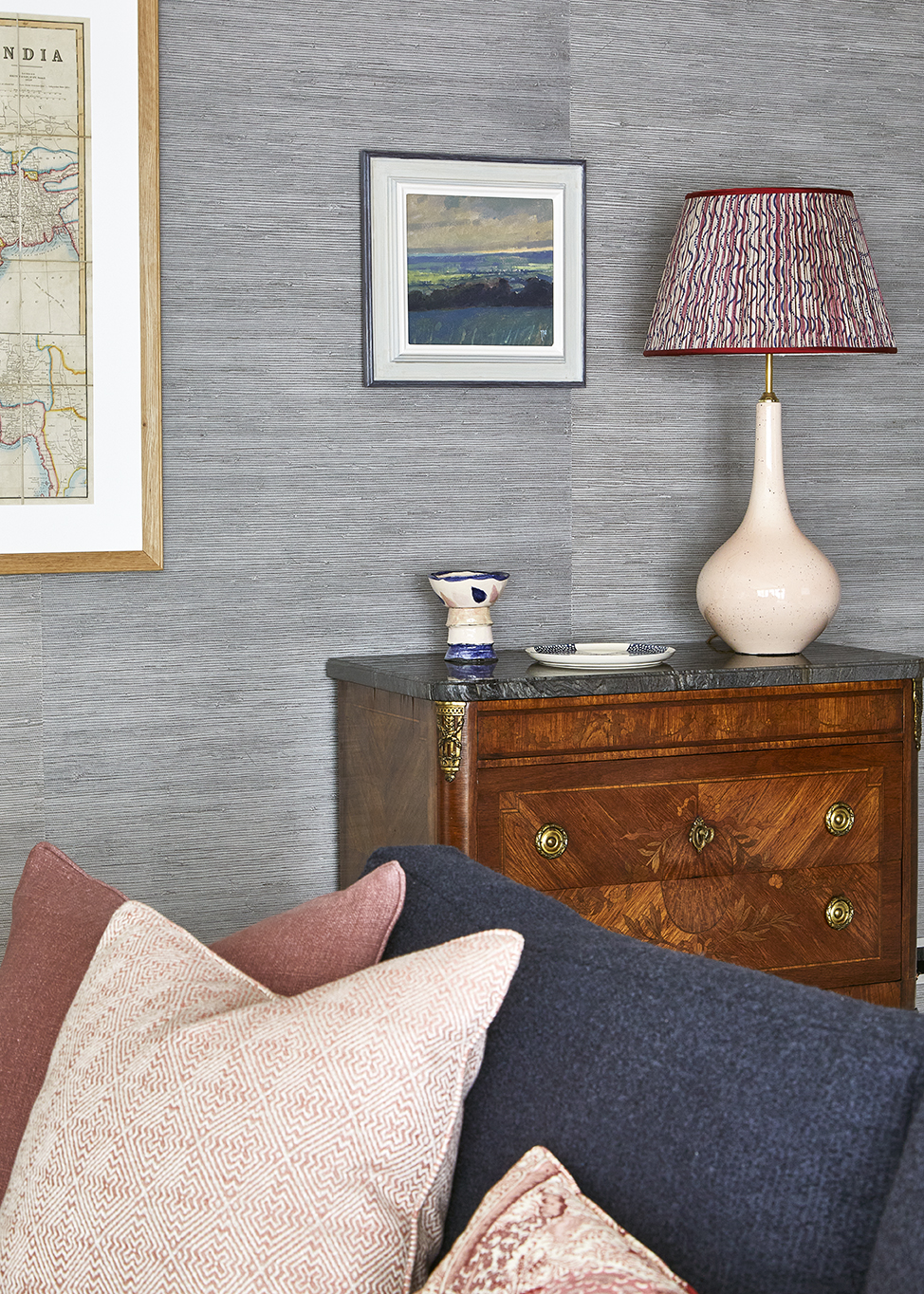 A living area with a wooden side table with a lamp and a painting above on the wall