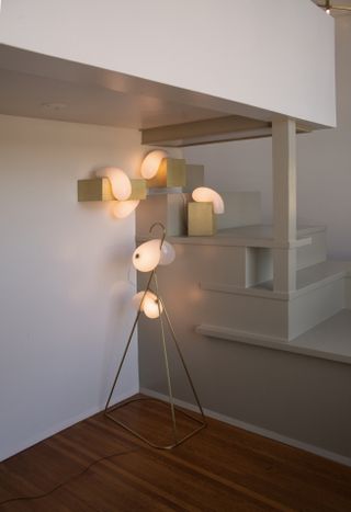 Wooden floor, white walls, white framed staircase, bespoke floor standing lighting, wall and stair light lit up, electric cable attached to light frame on the floor