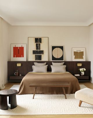 A bedroom with cream walls, taupe bedding and brown headboard