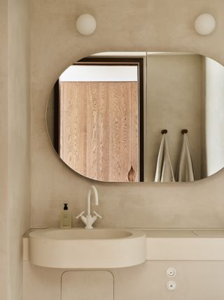 A minimalist bathroom with an oval mirror and lime-wash paint
